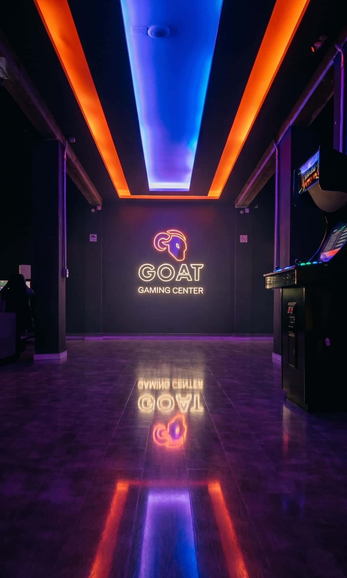 Entrada da GOAT Savassi com teto em neon laranja e roxo e o logo GOAT Gaming Center iluminado