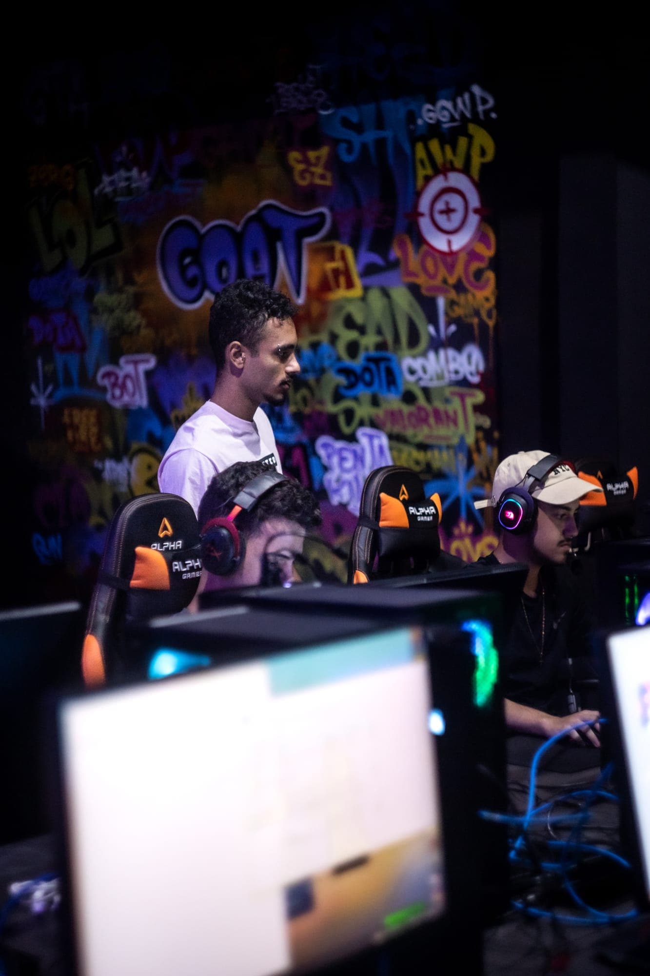 Jogadores competindo em campeonato de Counter-Strike 2 na GOAT, em frente à parede grafitada com o logo GOAT