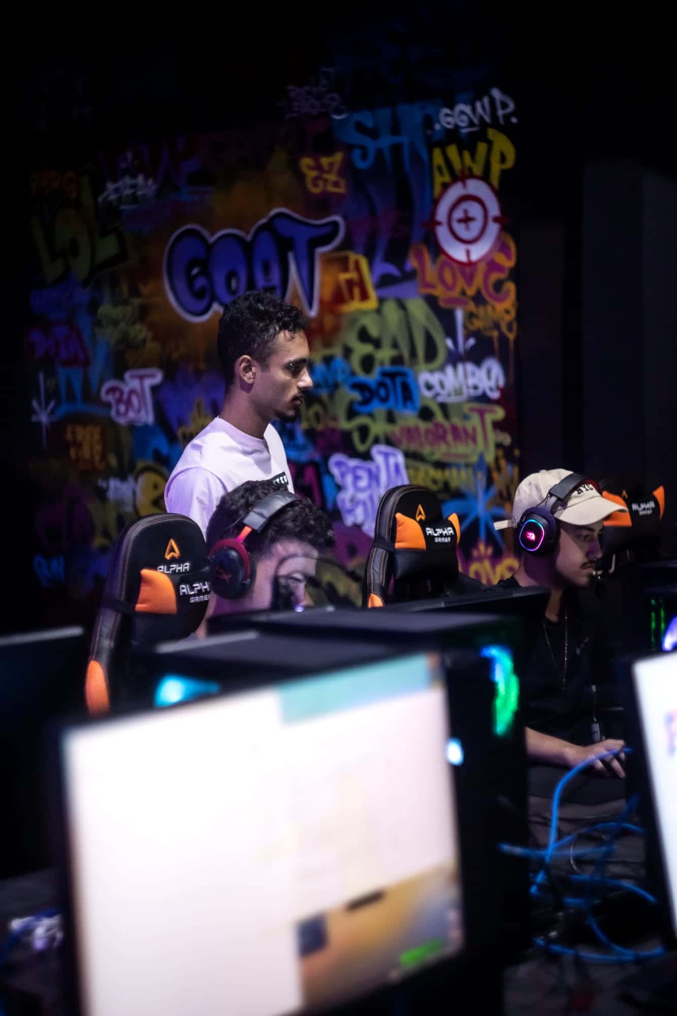 Jogadores competindo em campeonato de Counter-Strike 2 na GOAT, em frente à parede grafitada com o logo GOAT