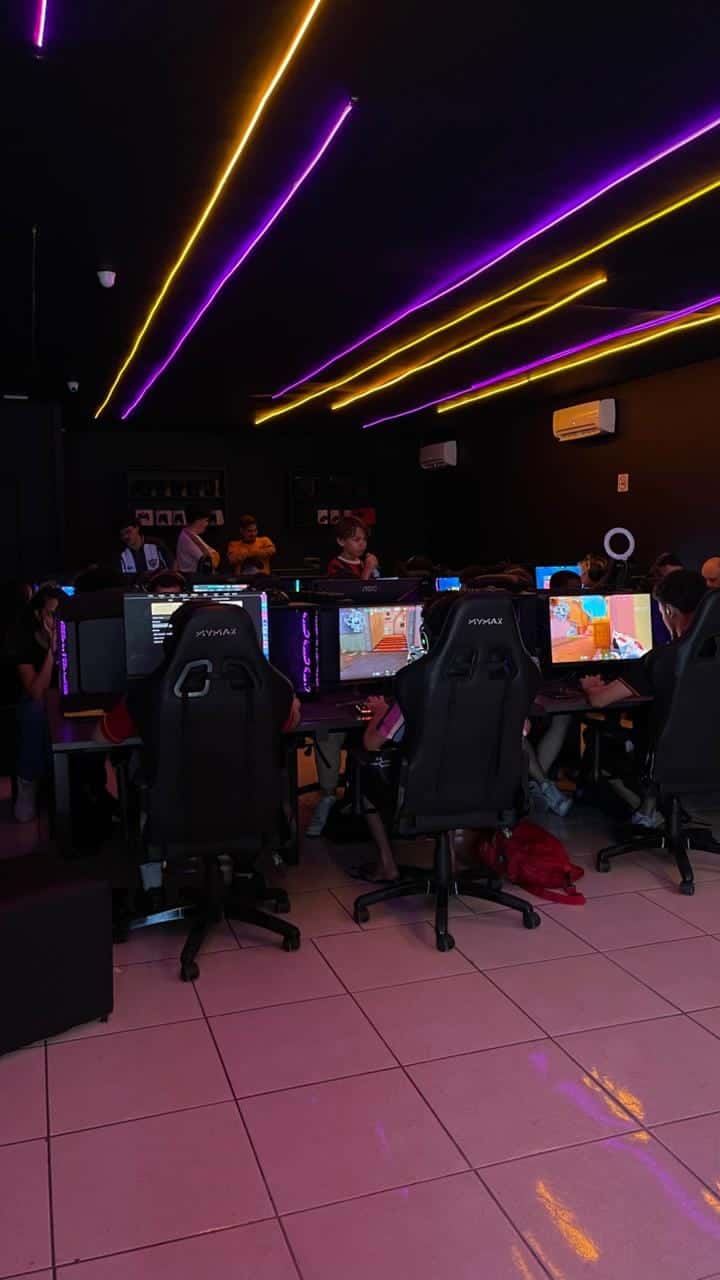Jogadores em PCs gamer durante evento de Valorant na GOAT, com luzes neon no teto