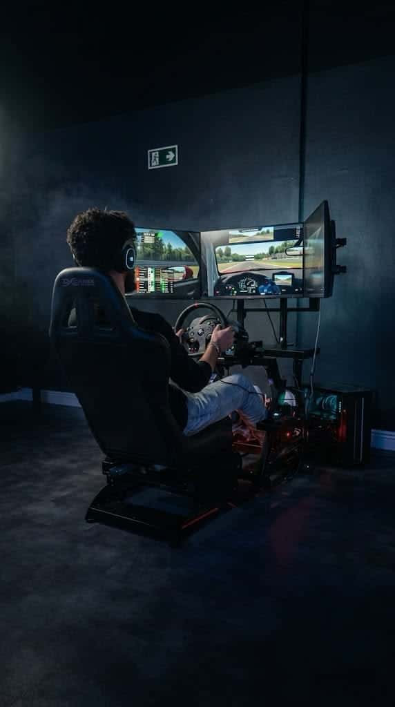 Jogador pilotando no simulador de corrida da GOAT, com volante, pedais, banco concha e três telas
